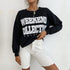 Close-up of black graphic sweatshirt with "Weekend Collective" text paired with white denim shorts and gold chain necklace