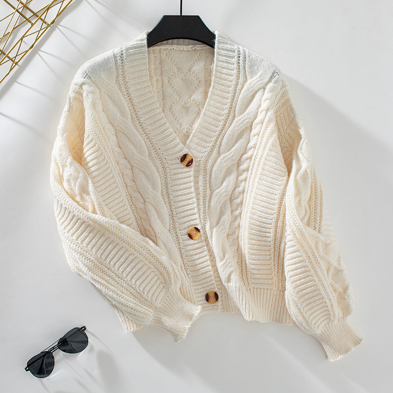 Ivory knit cardigan hanging on black hanger, showcasing textured fabric and design details