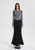 A woman is wearing a gray cropped hooded jacket with black accents and a black maxi skirt, standing straight against a white background