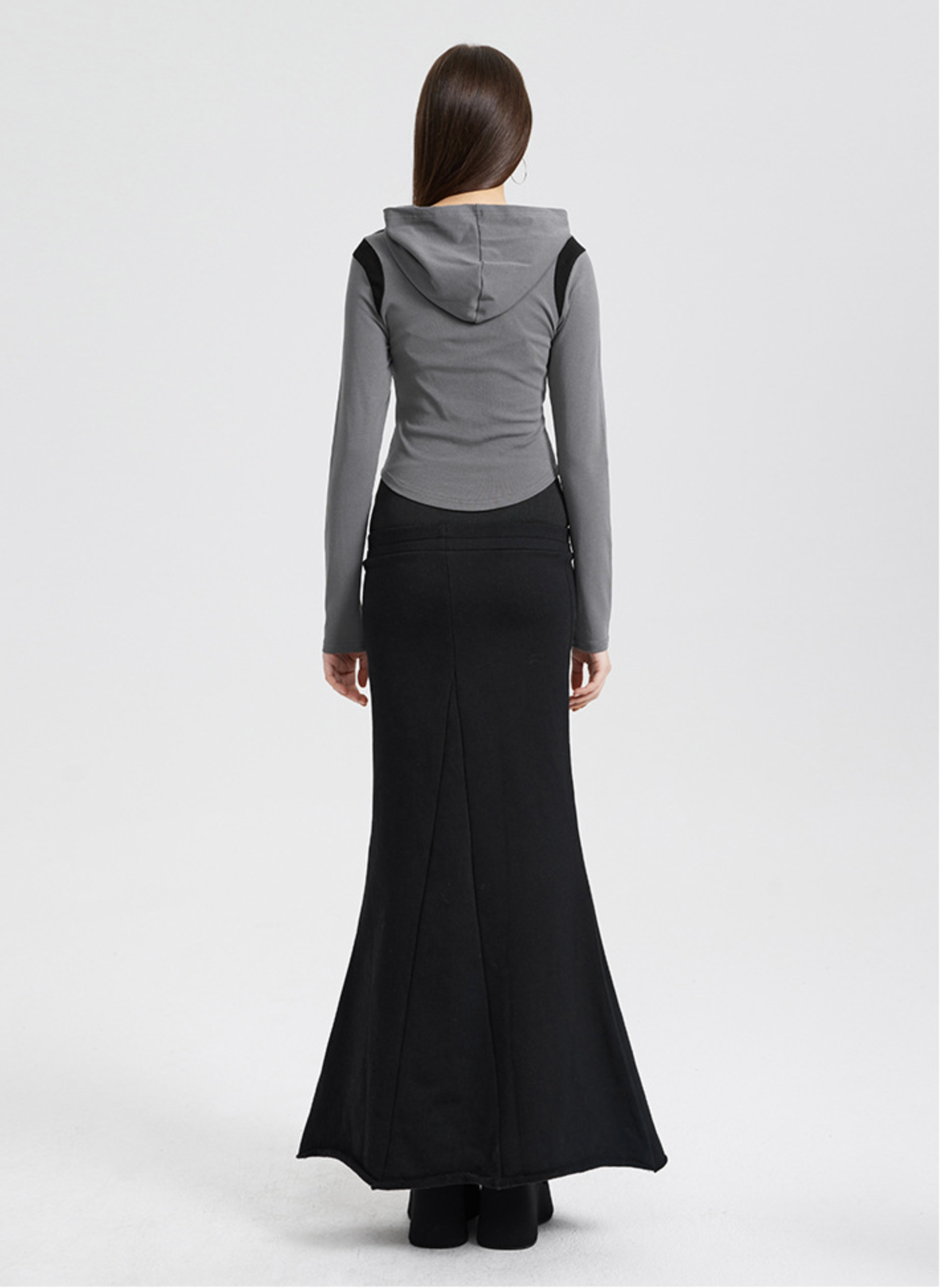 A woman is wearing a gray hooded crop top with black shoulder panels, showing the back view against a light gray background