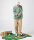 Full-length shot of sage green sweater with Balenciaga cap, khaki pants and white sneakers against white background