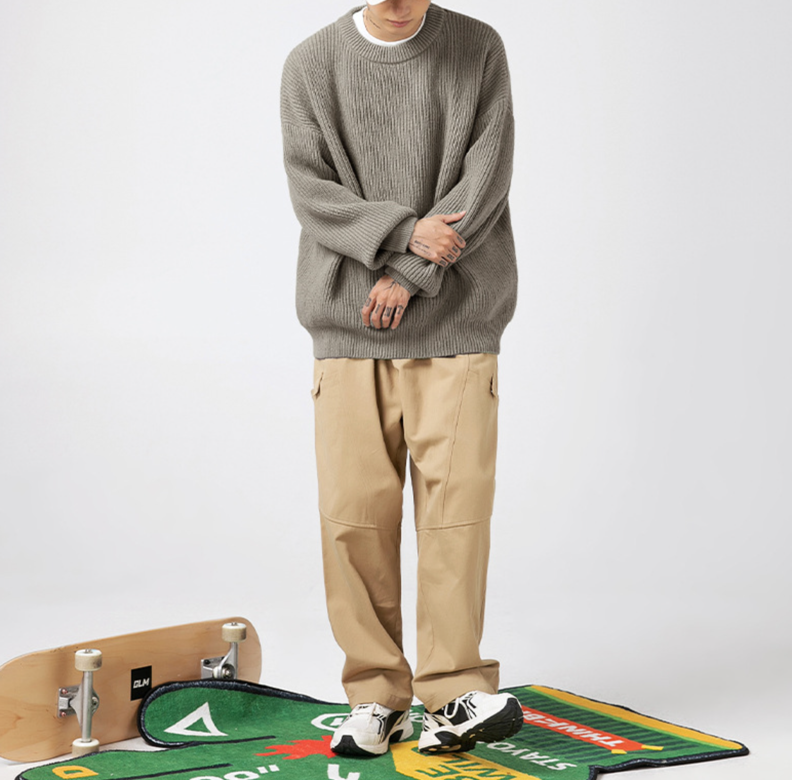 Light grey chunky knit sweater paired with khaki pants and skateboard accessories