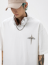 A man is looking down wearing white oversized tee with "FREEDOM" chest print. Features beige cap, white headphones and silver chain necklace