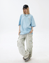 A woman is standing front-facing against white background. Wearing light blue oversized tee, black cap with blue logo and light beige cargo pants