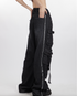 Side view of black distressed cargo pants with multiple pocket details and frayed edges, styled with grey crop top