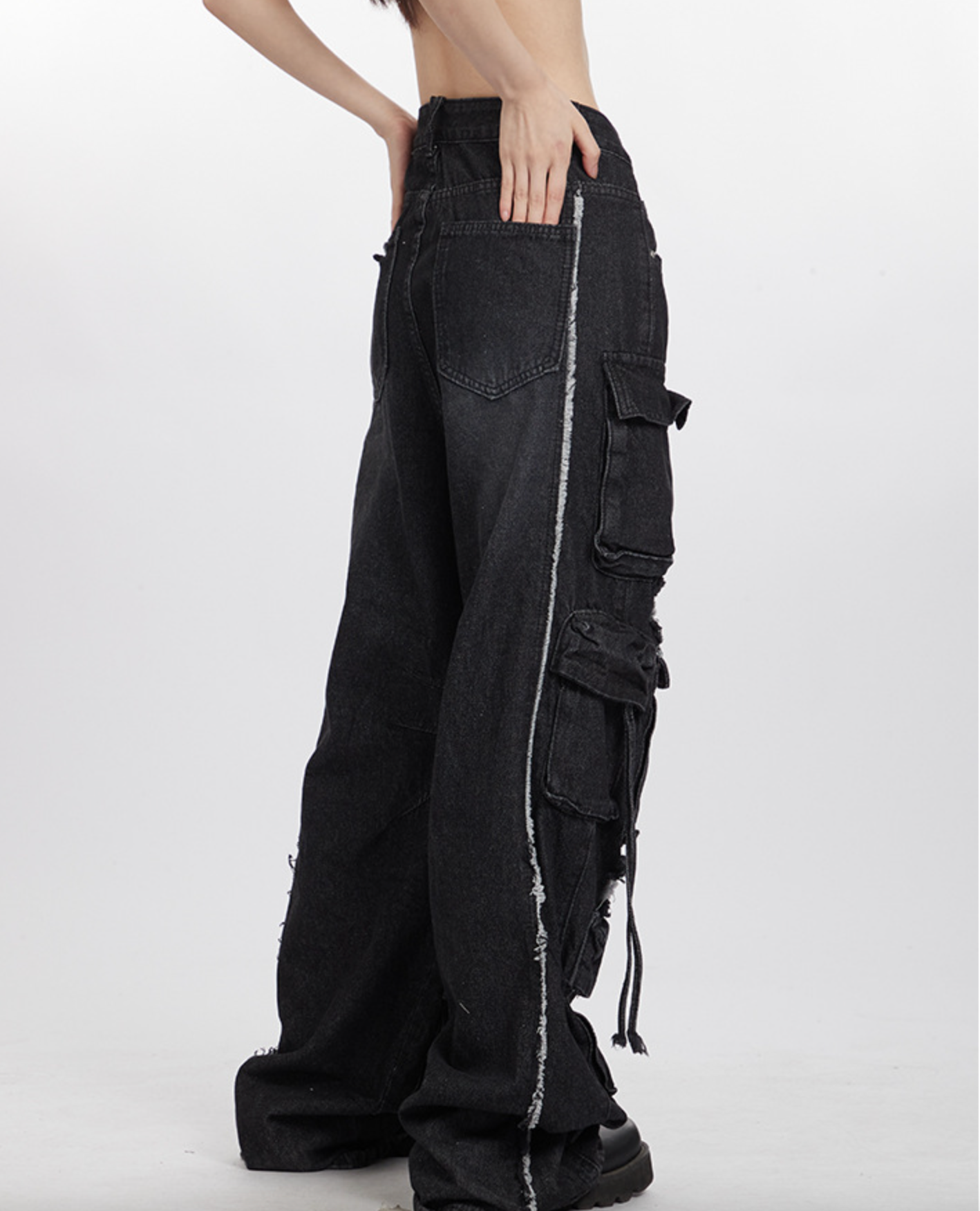 Side view of black distressed cargo pants with multiple pocket details and frayed edges, styled with grey crop top