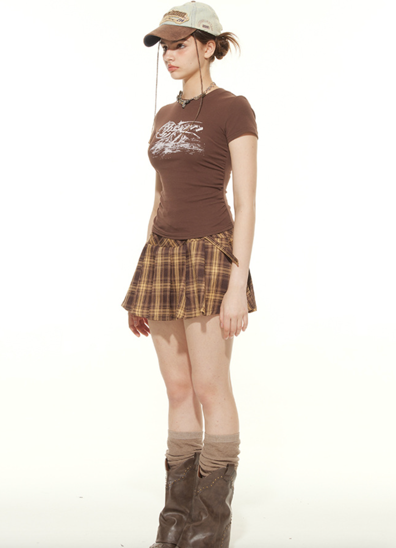 Side profile of fitted brown graphic tee with vintage baseball cap and plaid skirt look