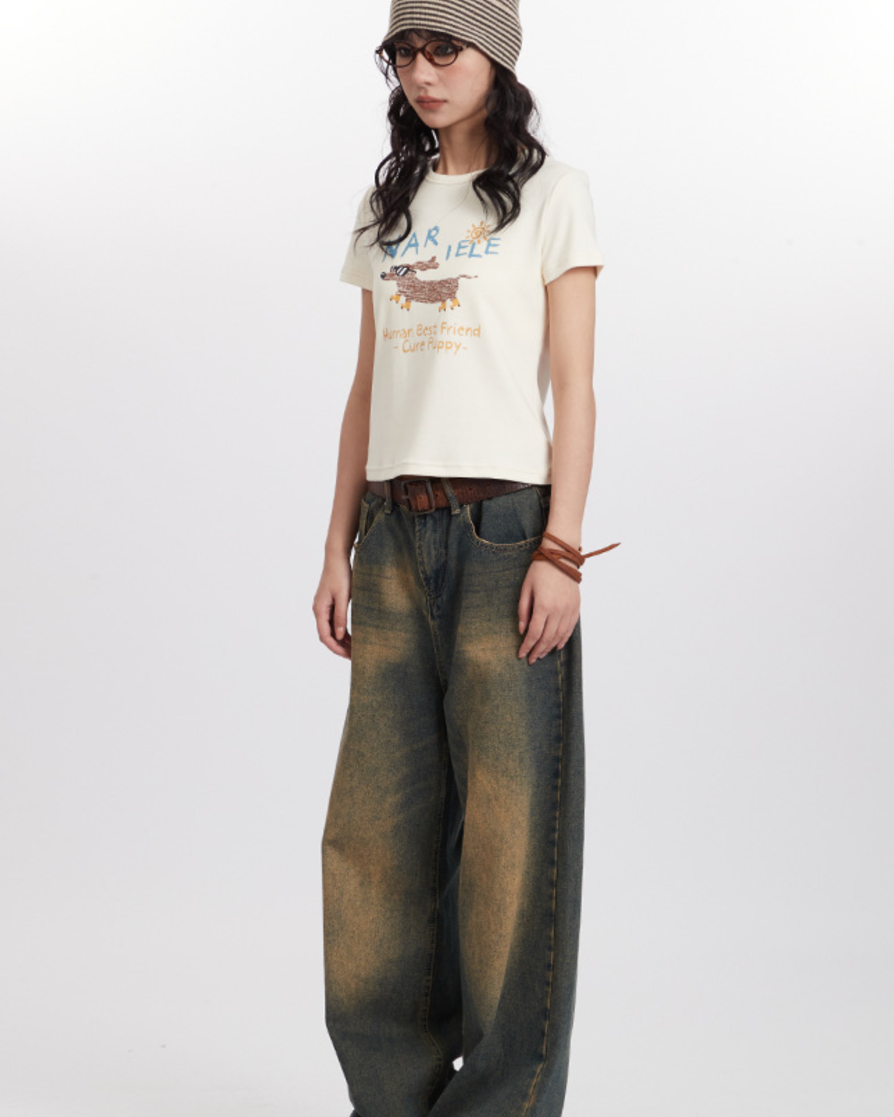 Model wearing vintage-inspired denim, dog graphic tee, striped hat in casual photoshoot
