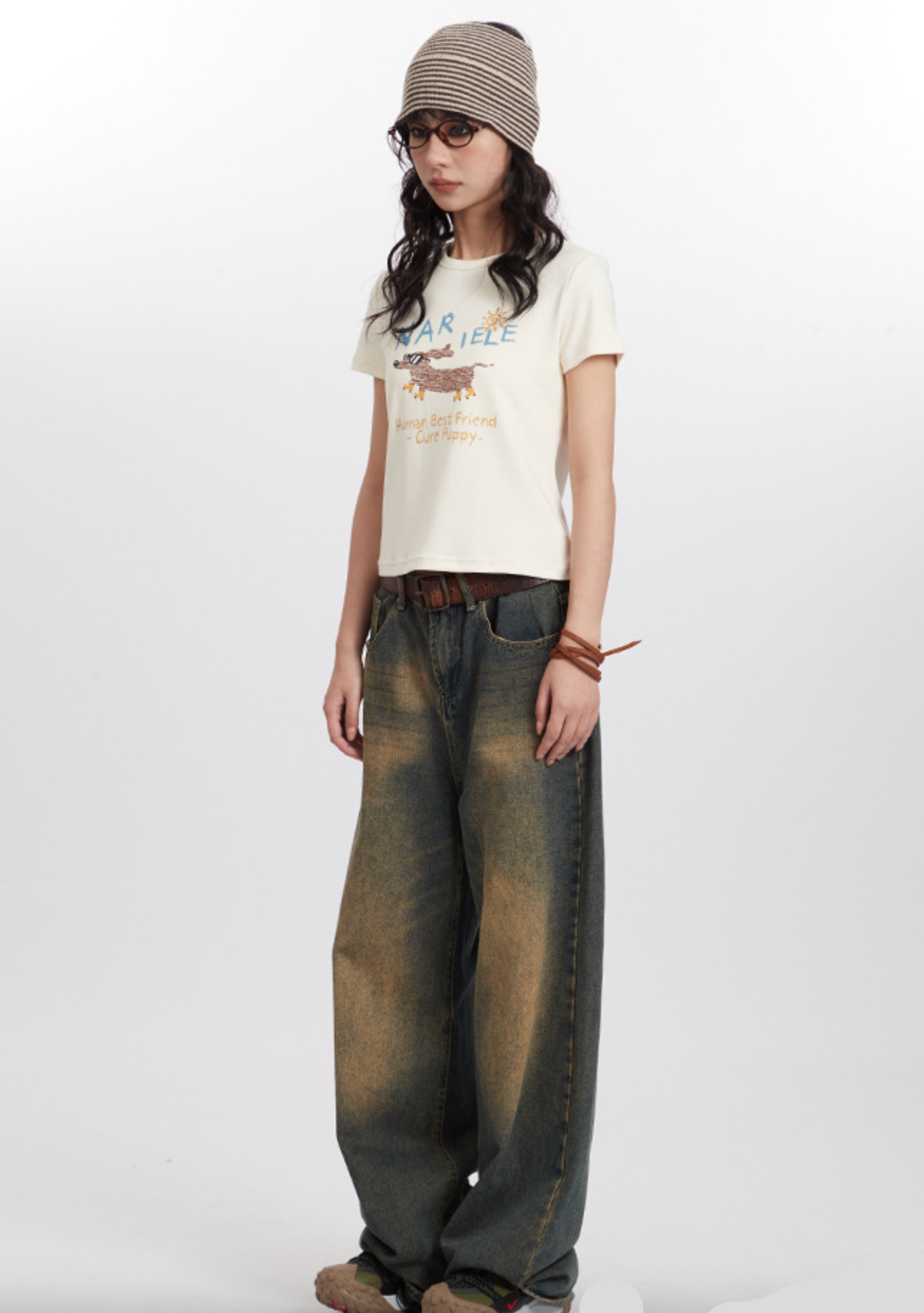 Model wearing vintage-inspired denim, dog graphic tee, striped hat in casual photoshoot
