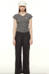 Woman wearing gray v-neck t-shirt with signature logo, black wide-leg pants and white military cap, full-length street style look