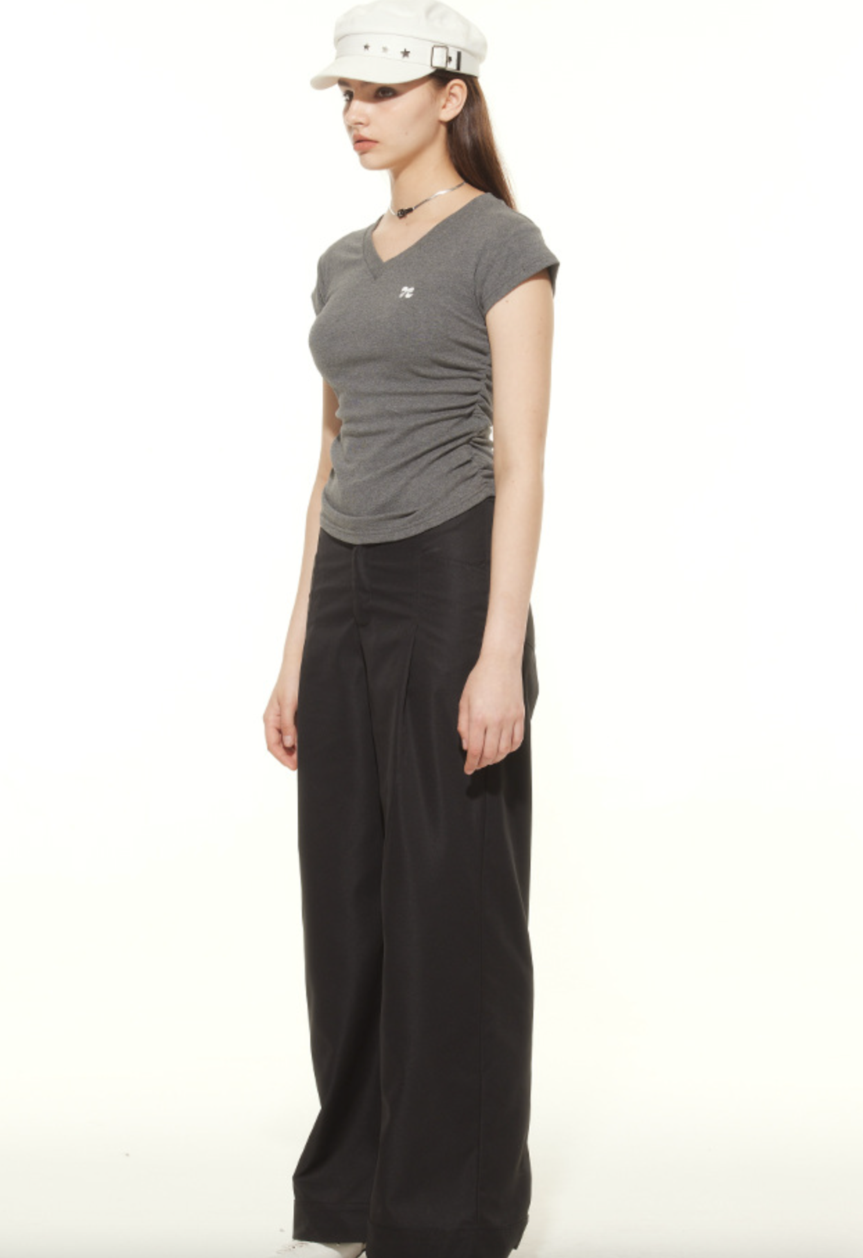Side profile of model in gray v-neck tee and black pants, styled with white military cap and minimalist choker necklace