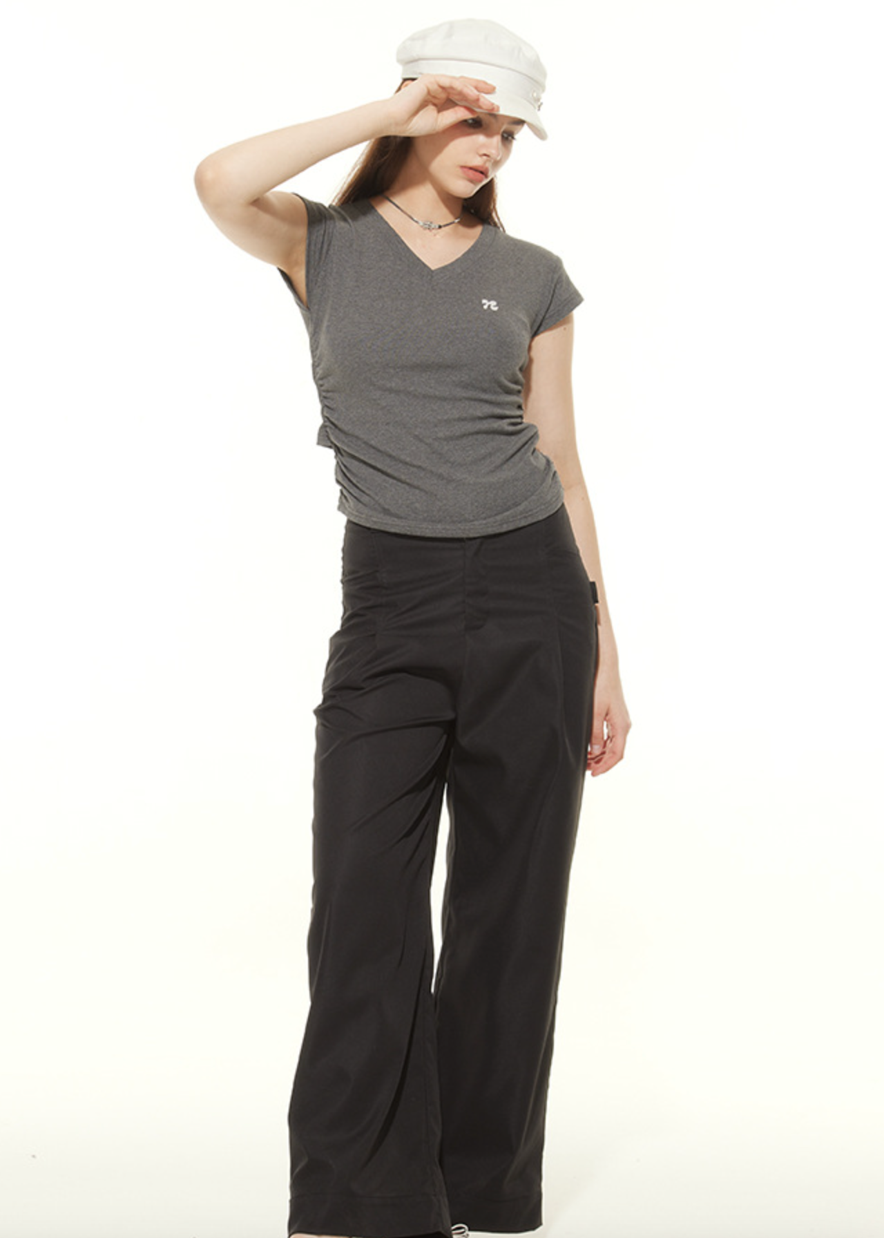 Model adjusting white cap wearing gray ruched t-shirt and black wide-leg pants, showcasing casual urban style