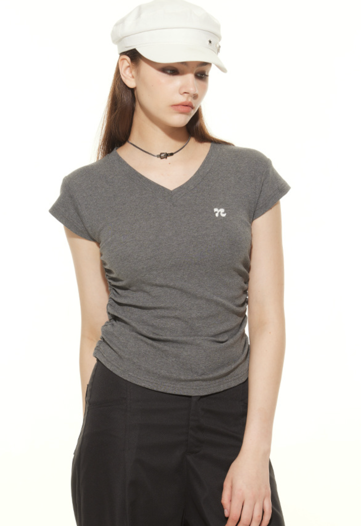 Close-up of gray v-neck t-shirt with small logo detail, styled with white military cap and delicate choker necklace