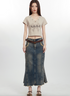 Young woman wearing beige crop top with abstract print, long denim skirt, and brown leather belt against white background