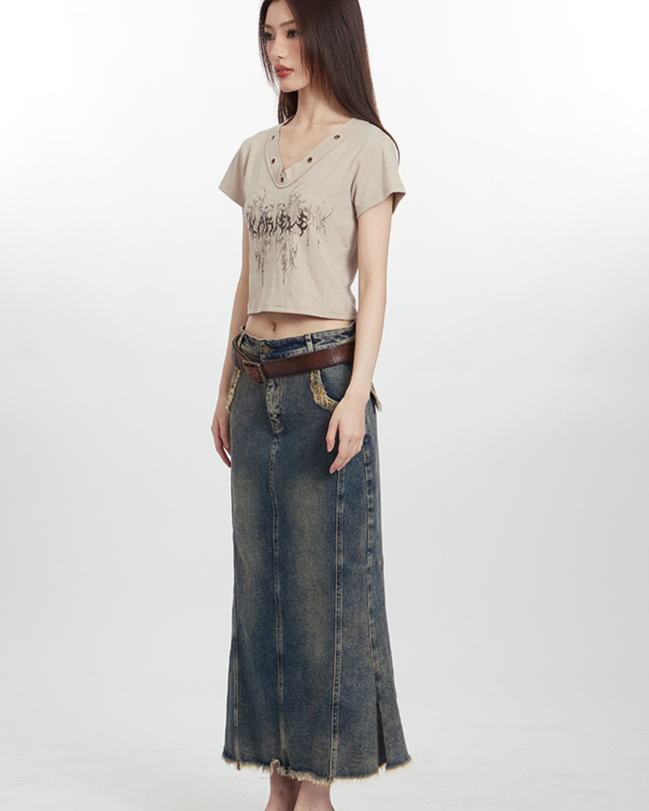 Side view of model in beige printed top and floor-length distressed denim skirt with frayed hem