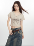 Close-up shot of woman in beige crop top with V-neck grommets and graphic print, paired with denim skirt