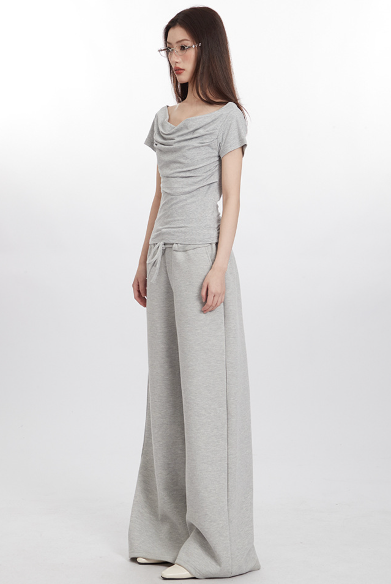 Side view of model in light gray draped top and wide-leg pants, wearing glasses