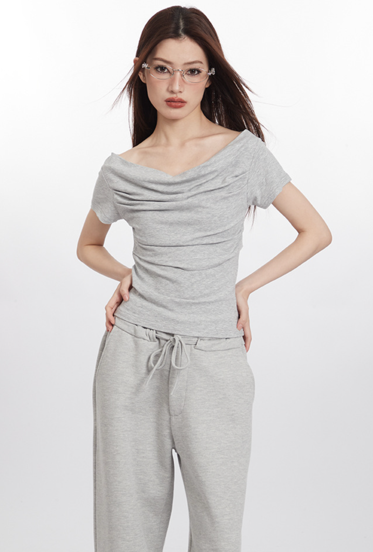 Full-body shot of model in light gray draped top and wide-leg pants, wearing glasses