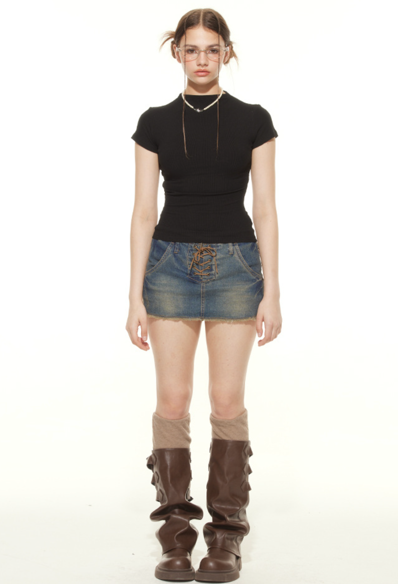Model wearing black fitted mock neck tee with lace-up denim mini skirt and brown combat boots, accessorized with glasses