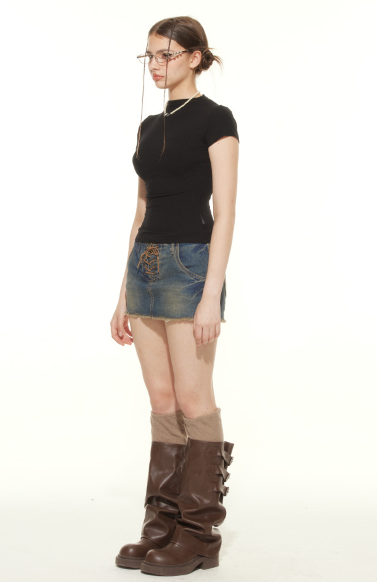 Side profile of model in black fitted t-shirt and lace-up denim skirt, styled with vintage glasses and combat boots