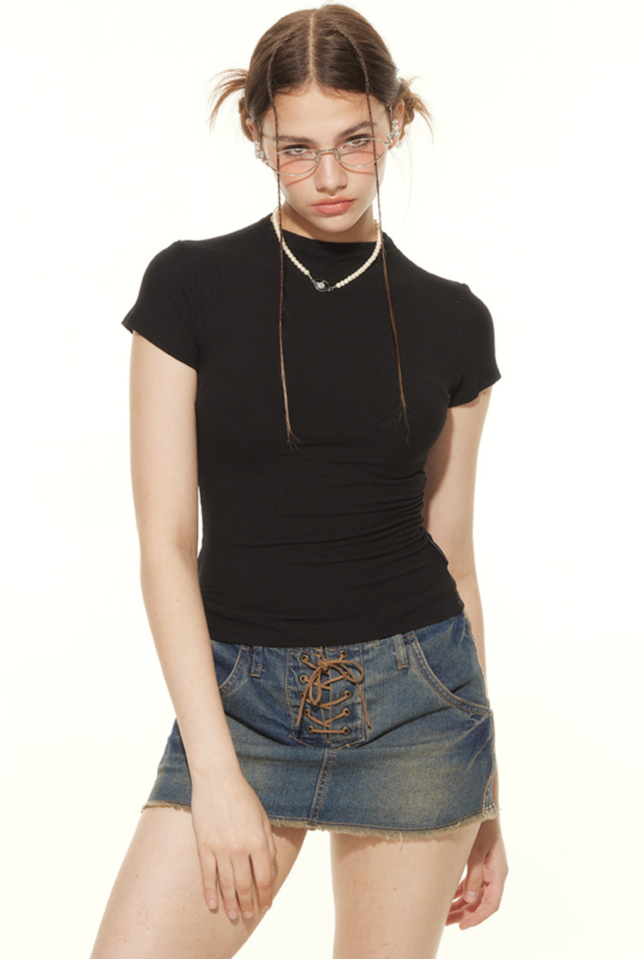 Model wearing fitted black tee and lace-up denim skirt, styled with vintage accessories and statement pose