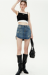 A woman is adjusting sunglasses while wearing a black contrasting-trim crop top, distressed denim mini skirt and knee-high boots with black bag