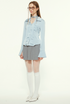 Woman in light blue blouse, gray pleated skirt, glasses, white tights, white shoes