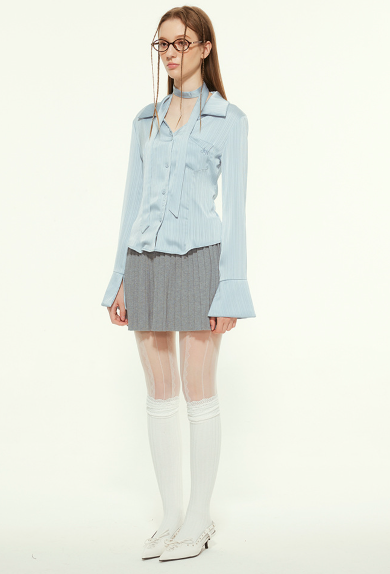 Woman in light blue blouse, gray pleated skirt, glasses, white tights, white shoes