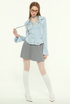 Woman in light blue blouse, playing with hair, gray pleated skirt, white tights