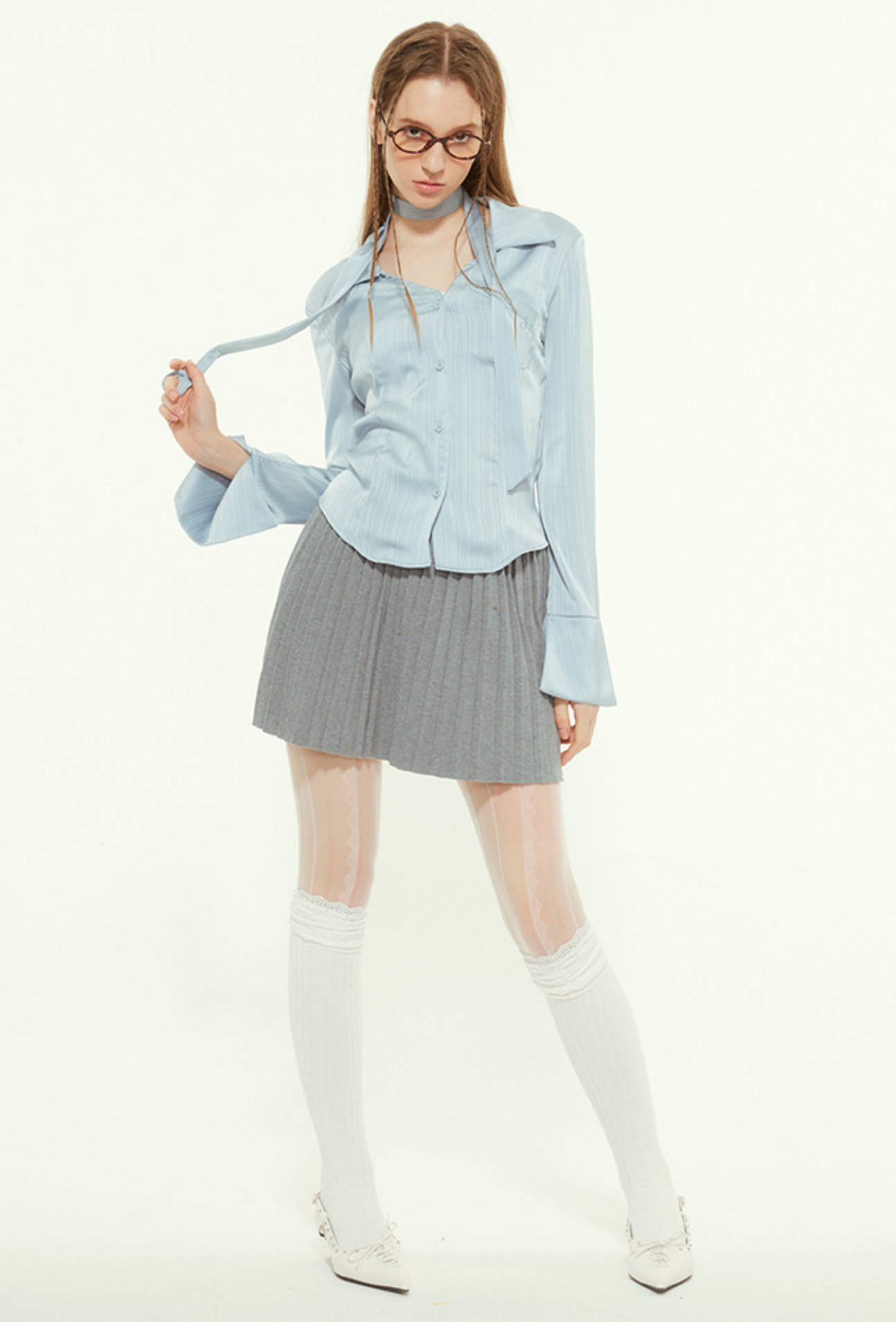 Woman in light blue blouse, playing with hair, gray pleated skirt, white tights