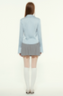 Back view of woman in light blue blouse and pleated skirt, white tights, white shoes