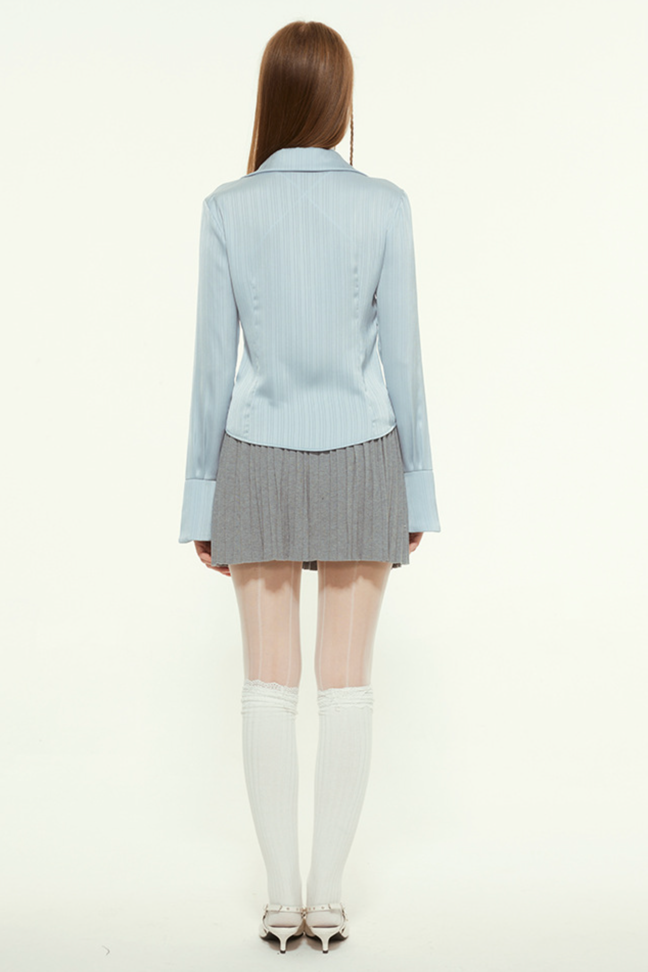 Back view of woman in light blue blouse and pleated skirt, white tights, white shoes