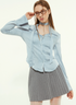 Woman in light blue blouse, adjusting glasses, gray pleated skirt, white tights