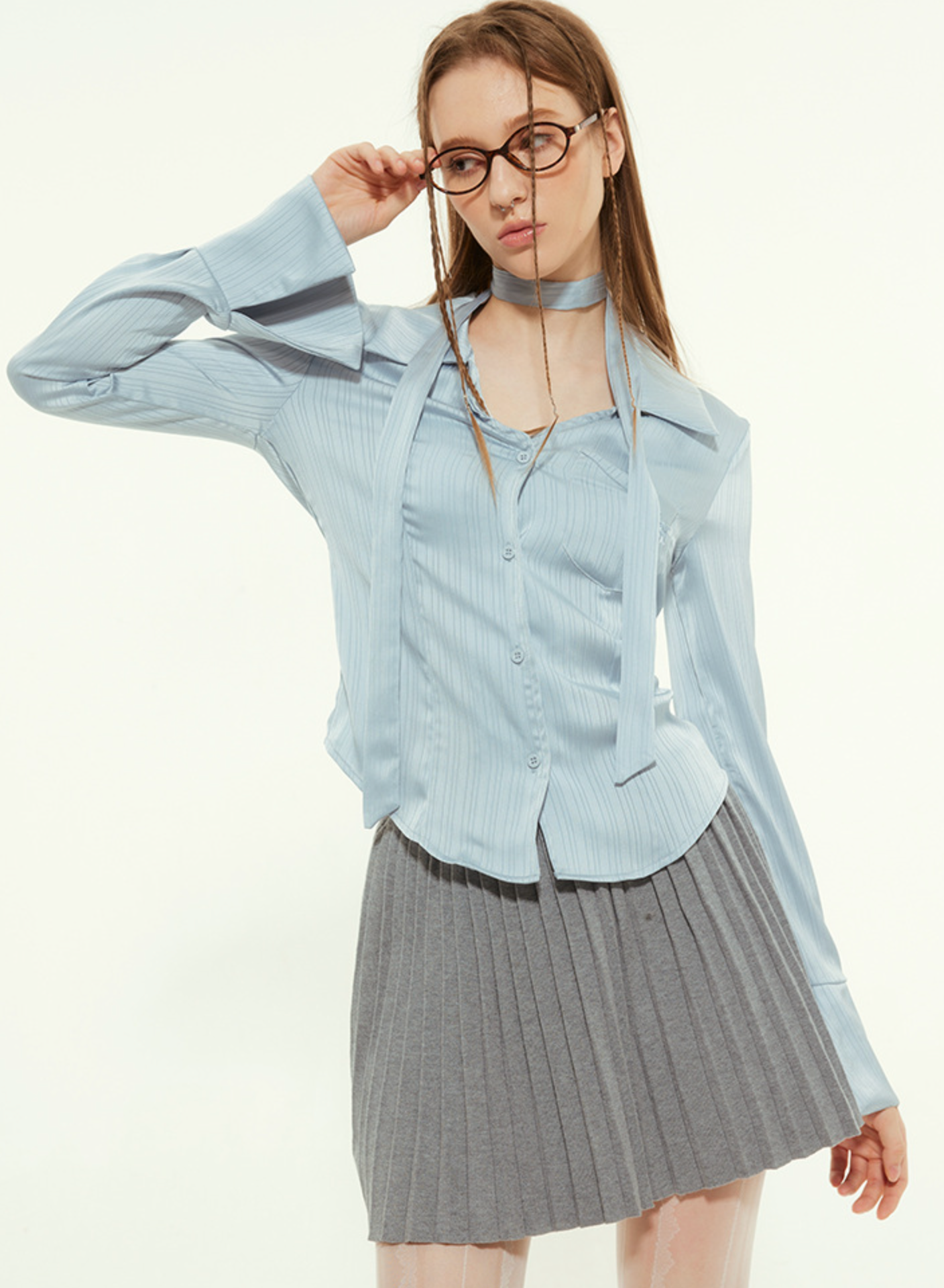 Woman in light blue blouse, adjusting glasses, gray pleated skirt, white tights