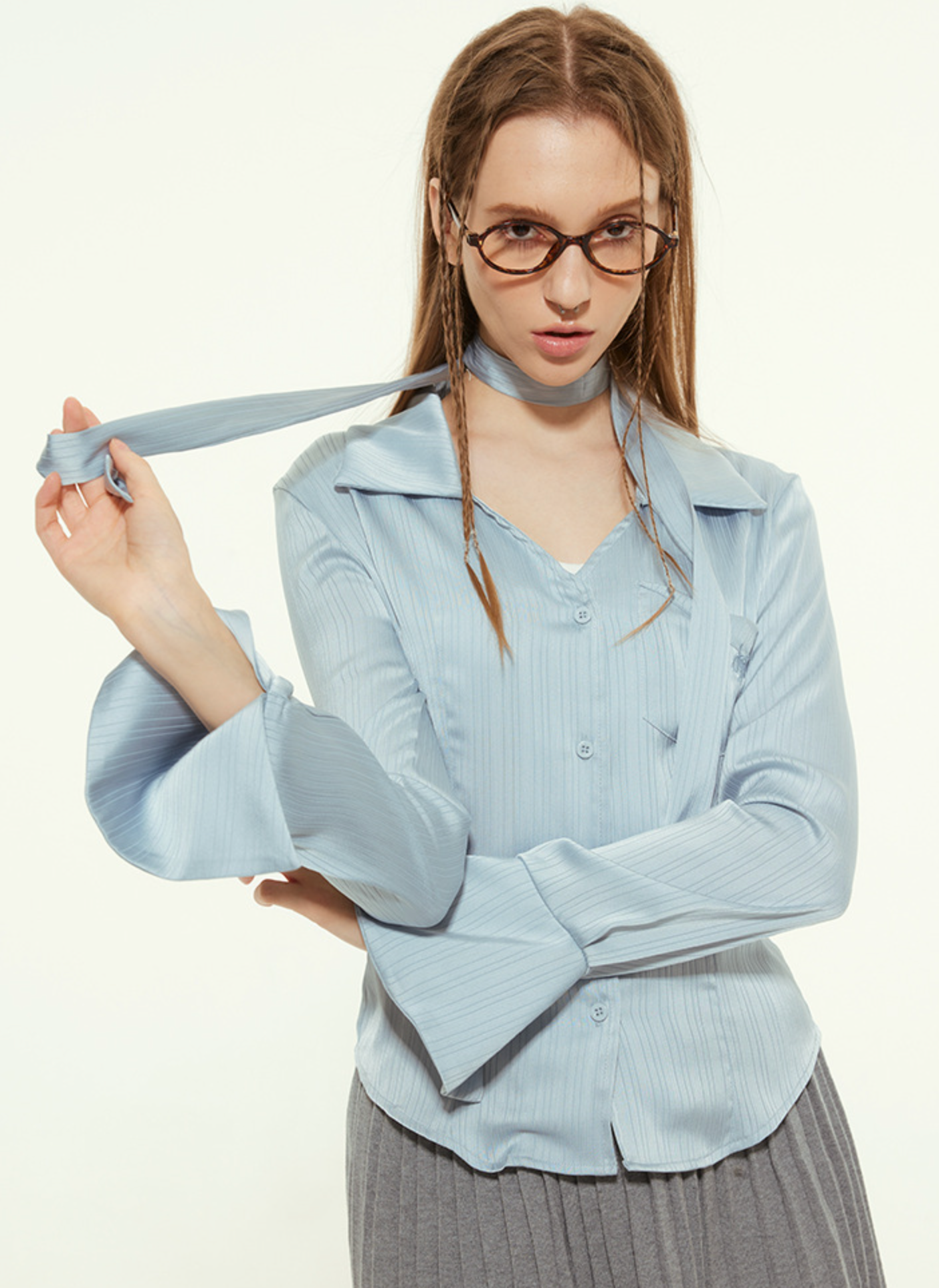 Woman in light blue blouse, holding choker, glasses, gray pleated skirt