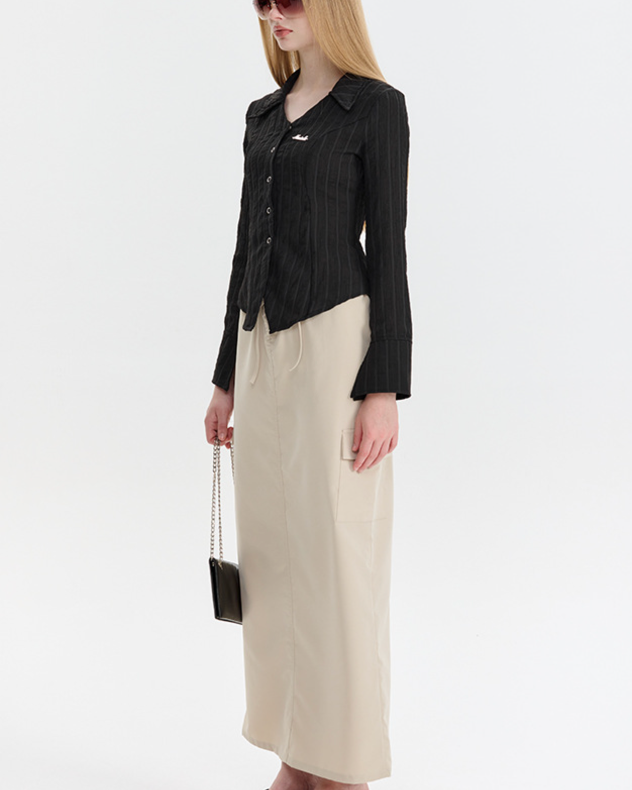 A model is standing in profile wearing a black pinstriped blouse, beige wide-leg pants, platform flip-flops, and rose-tinted sunglasses
