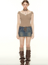 A woman wearing a tan ribbed crop top with white trim and lace-up denim mini skirt stands with brown knee-high boots against white background