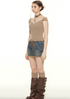 A woman wearing a beige ribbed cap sleeve top with white trim stands in profile, paired with lace-up denim skirt and brown boots