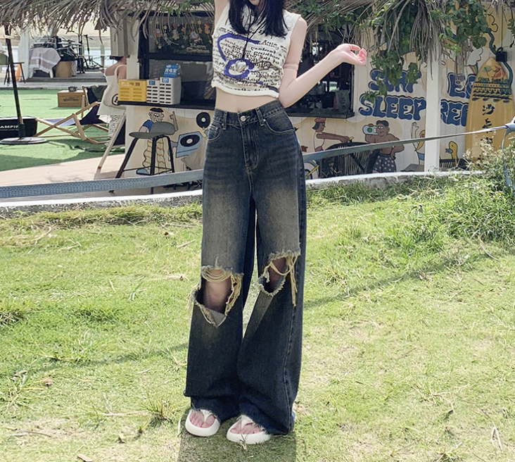 Full body view of woman in printed crop top and ripped wide-leg jeans at outdoor venue