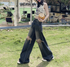 Woman in printed crop top and distressed jeans walking on grass, outdoor cafe setting visible