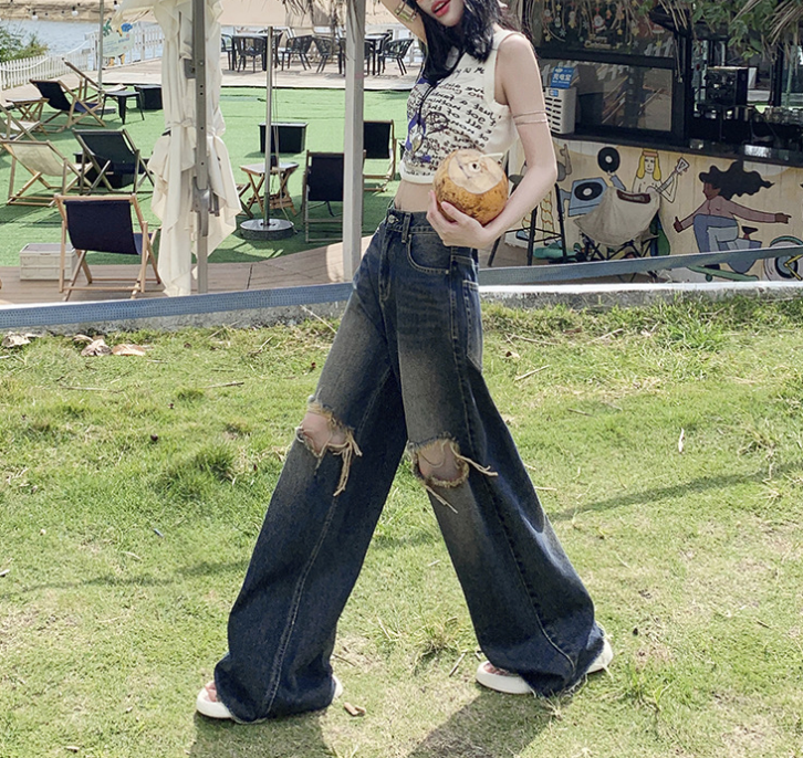 Woman in printed crop top and distressed jeans walking on grass, outdoor cafe setting visible