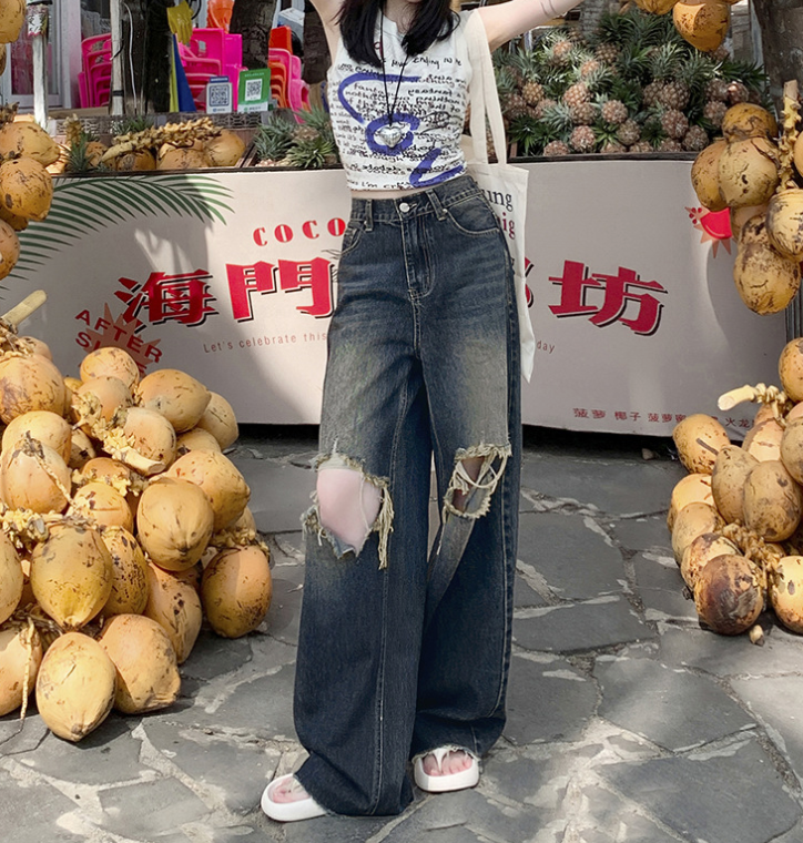 Woman in white graphic top and ripped jeans standing between piles of fresh coconuts at Asian market
