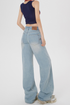 Back view of model in wide-leg light wash jeans showing YC branding on back pocket, paired with crop top and sneakers
