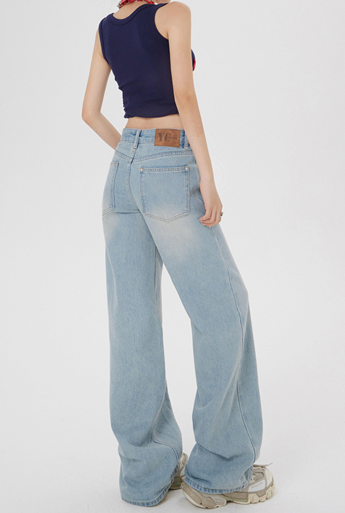 Back view of model in wide-leg light wash jeans showing YC branding on back pocket, paired with crop top and sneakers