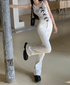 A woman kicks up one leg while wearing white flare jeans and a bow-detailed tank top, posed against a concrete pillar