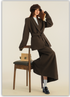 Model seated on wooden chair wearing brown wool suit set with newsboy cap and loafers