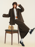 Editorial pose showing relaxed fit brown suit with vintage chair and minimalist styling