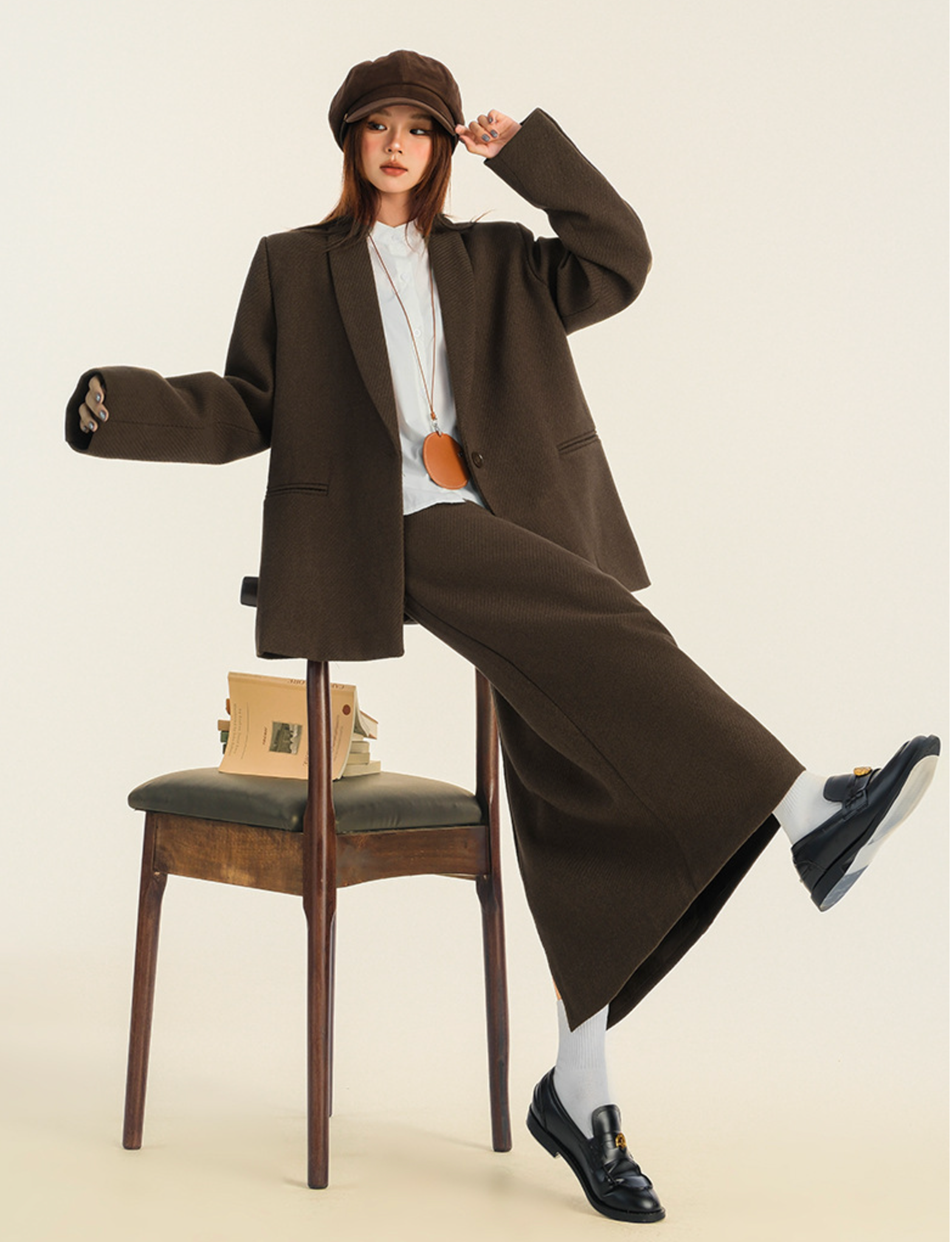 Editorial pose showing relaxed fit brown suit with vintage chair and minimalist styling