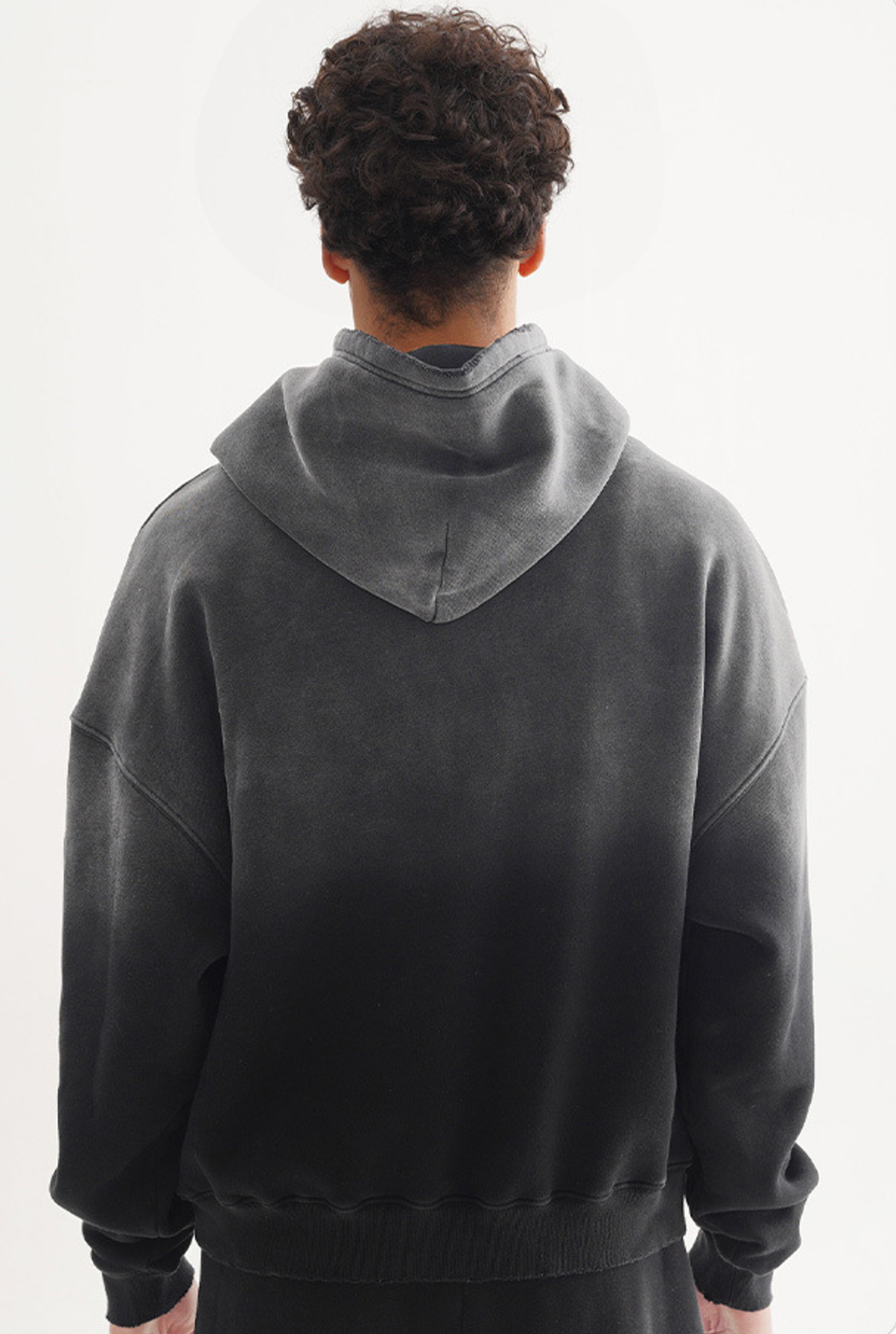 Back view of model in grey-to-black gradient hoodie with drop shoulders showing ombre effect, against white background