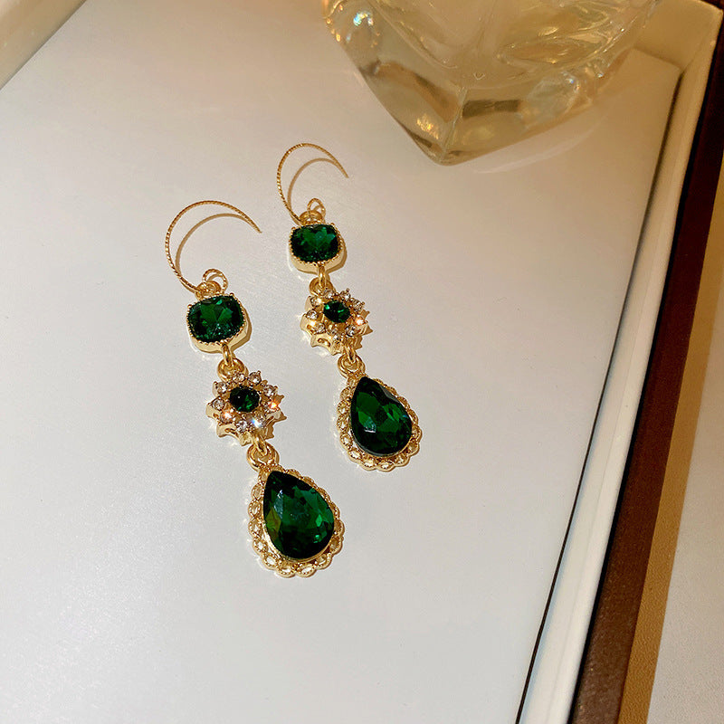 Elegant gold drop earrings with emerald green gemstones, featuring teardrop and round cut stones with intricate golden settings